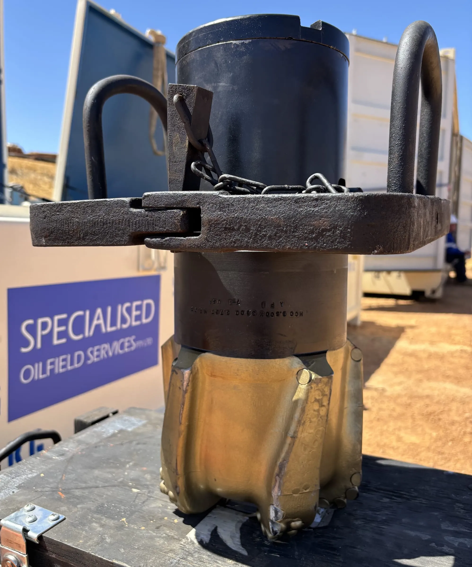 Close-up of a PDC core head on a core barrel, SOS sign behind