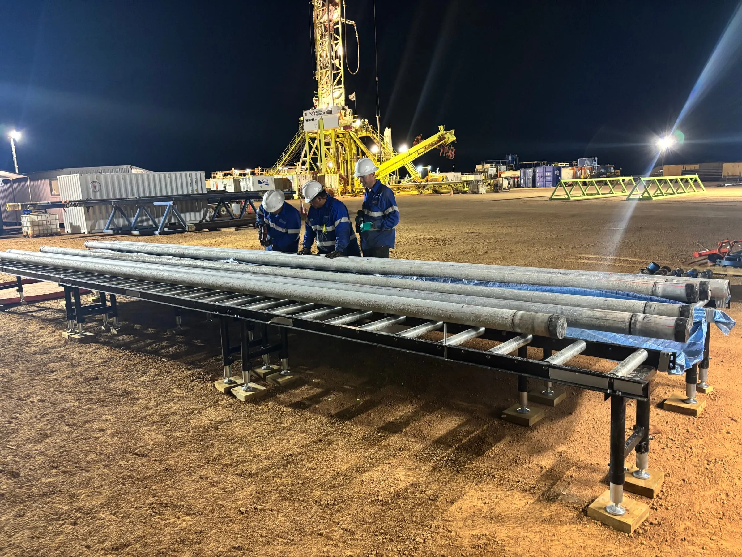 Crew laying out core along the processing tables at night, the rig lit behind them