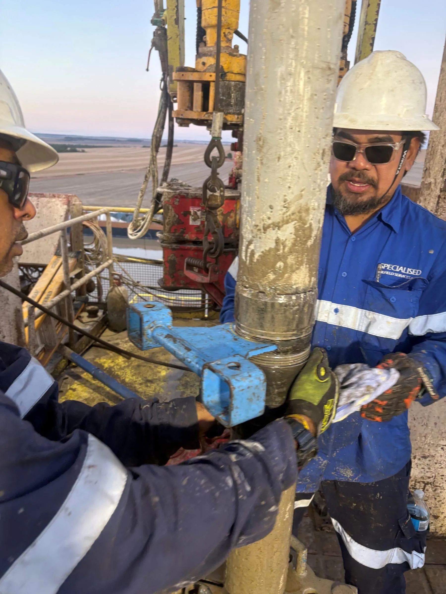 Two SOS engineers working a clamp on the core barrel at the rig floor