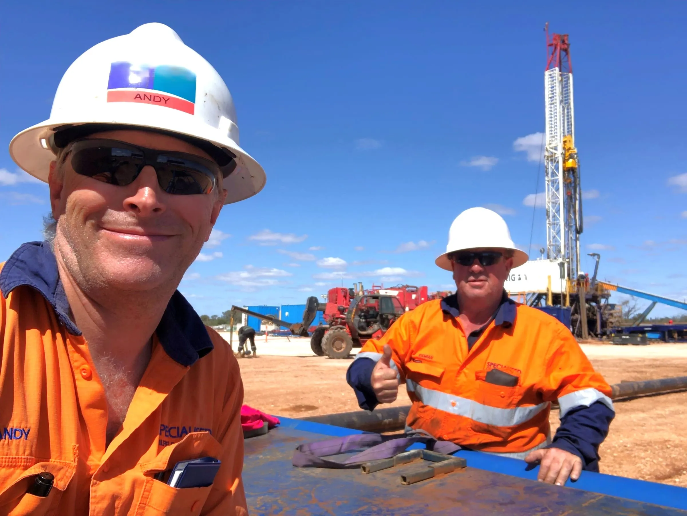 Two SOS coring engineers at an onshore rig site, the derrick behind them