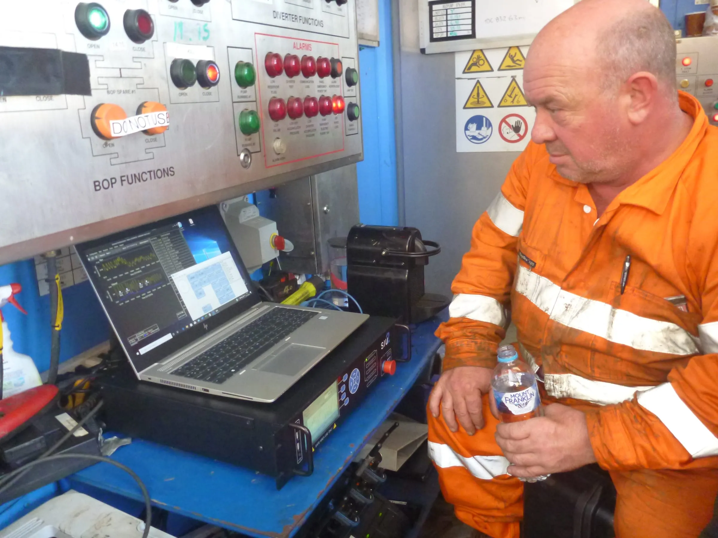 Coring engineer watching SureCore data on a laptop beside the BOP control panel at the rig floor